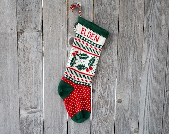 May include: A red and green knitted Christmas stocking with a white holly pattern and the name "Elden" embroidered on the front.