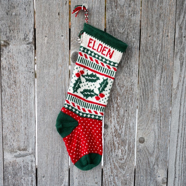 May include: A red and green knitted Christmas stocking with a white holly pattern and the name "Elden" embroidered on the front.