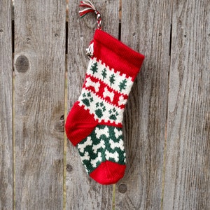 May include: A red and green knitted Christmas stocking with a white paw print and bone pattern hanging on a weathered wooden fence.