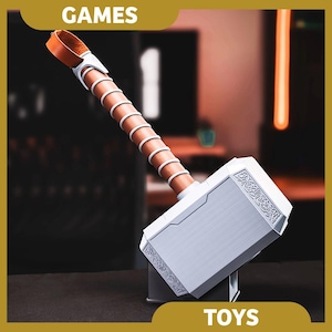 May include: A toy hammer with a white head and a brown handle wrapped in white and brown bands. The hammer has a leather strap and is labeled "TOYS" and "GAMES".