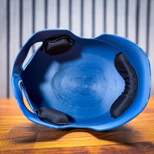 May include: A blue baseball helmet with black padding inside. The helmet is made of a hard plastic material and has a smooth, curved design. The interior features three black padded cushions for comfort and protection.