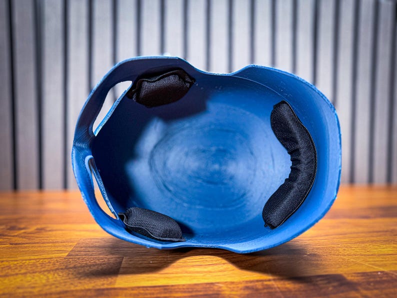 May include: A blue baseball helmet with black padding inside. The helmet is made of a hard plastic material and has a smooth, curved design. The interior features three black padded cushions for comfort and protection.