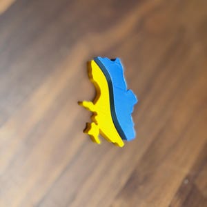 May include: A 3D-printed object in the shape of a country, featuring a blue and yellow color scheme. The object is likely a decorative item or a souvenir, possibly representing a specific region or nation.