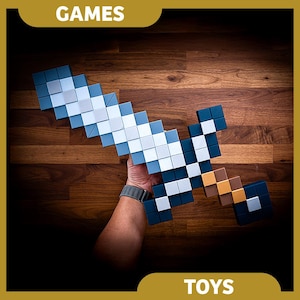 May include: A blue and white plastic Minecraft sword toy. The sword is made up of small square blocks and has a brown handle. The sword is held in a person's hand against a wooden background.