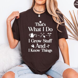 May include: Dark chocolate brown t-shirt with the text "That's What I Do, I Grow Stuff And I Know Things" in white. The shirt features gardening-related icons. The model is wearing light blue jeans.