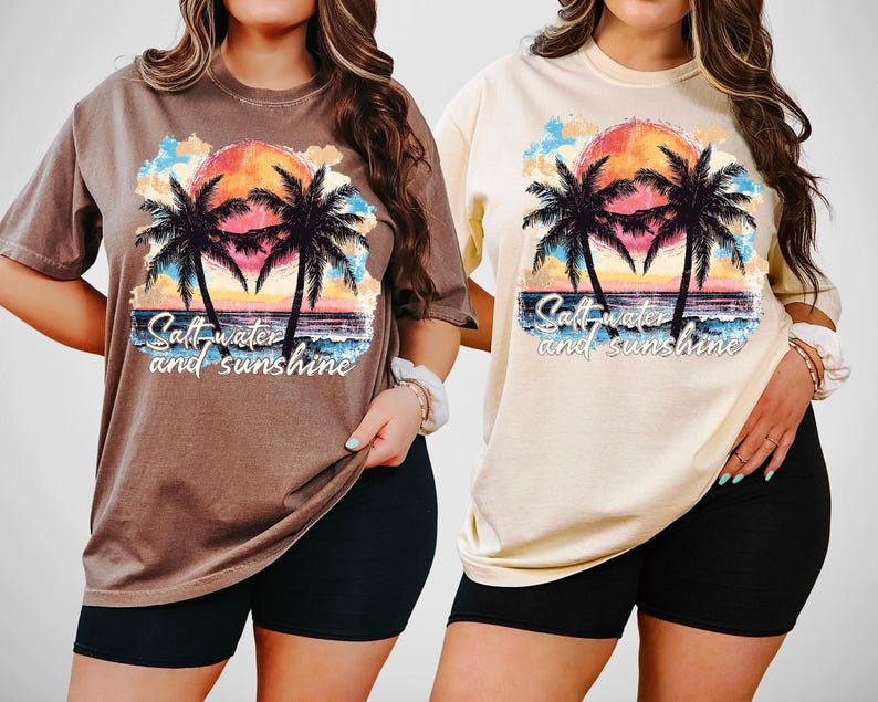 Puede incluir: Dos camisetas, una marr&oacute;n y otra crema, con un dise&ntilde;o de puesta de sol tropical. El gr&aacute;fico muestra palmeras, una colorida puesta de sol, olas del oc&eacute;ano y el texto "Salt water and sunshine".