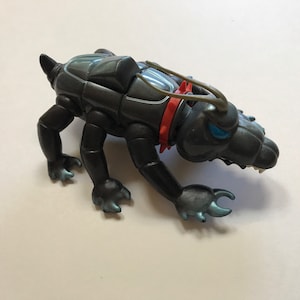 May include: A black plastic toy dog with a red collar and blue eyes. The dog has a segmented body and a long tail.