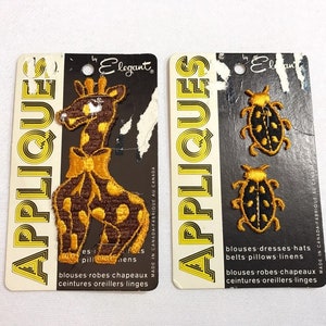 May include: Two cards with the word "Appliques" printed on them in yellow letters. The card on the left has a brown and yellow giraffe applique with a bow tie. The card on the right has two black and yellow ladybug appliques. Both cards have the text "Made in Canada Fabrique au Canada" printed on them.