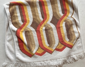 May include: White beach towel with a fringe border and a geometric pattern in orange, yellow, and brown.