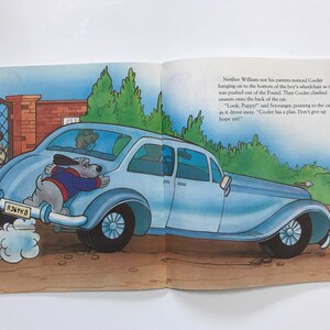 May include: A blue car with a dog hanging out of the back. The dog is wearing a blue sweater and has a white collar. The car has a license plate that reads "R367KB".