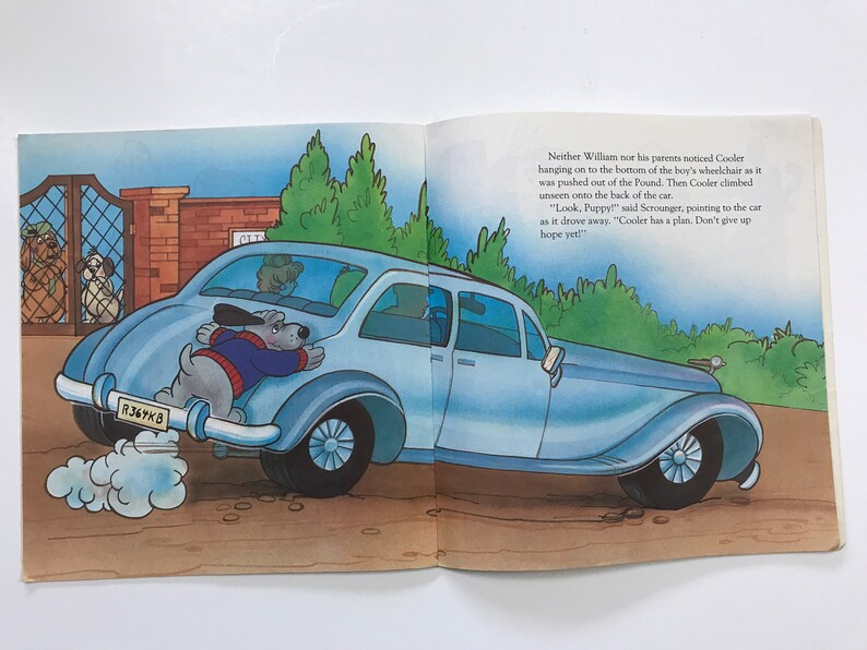 May include: A blue car with a dog hanging out of the back. The dog is wearing a blue sweater and has a white collar. The car has a license plate that reads "R367KB".