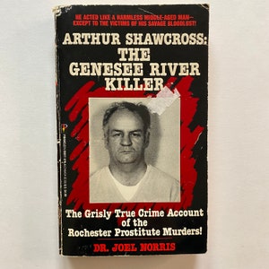 May include: A book cover with a red background and white text. The title is "Arthur Shawcross: The Genesee River Killer." The cover features a black and white photo of a man with a serious expression. The text below the photo reads "The Grisly True Crime Account of the Rochester Prostitute Murders!" and "Dr. Joel Norris."