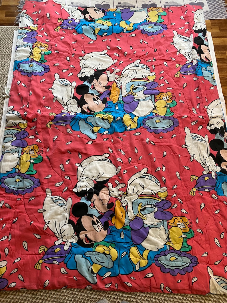 May include: A red and white quilt with a repeating pattern of Mickey Mouse and Donald Duck. The characters are surrounded by white flower petals.