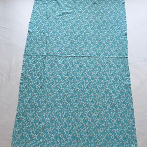 May include: A light blue fabric with a white and pink floral pattern. The fabric is folded in half and laid flat on a white surface.