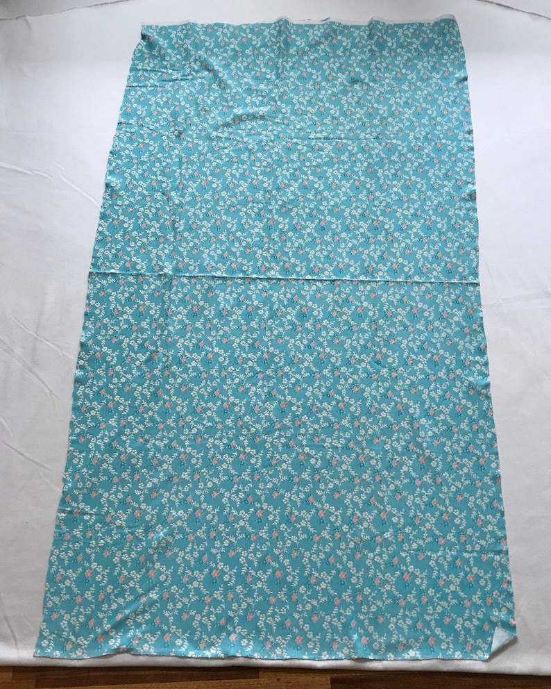 May include: A light blue fabric with a white and pink floral pattern. The fabric is folded in half and laid flat on a white surface.
