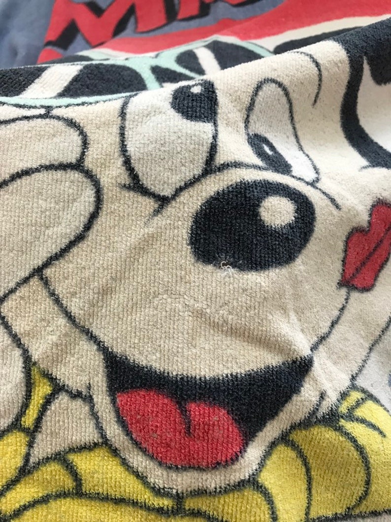 Pode incluir: Close-up do rosto de um c&atilde;o de desenho animado em uma toalha. O c&atilde;o tem um nariz preto, olhos pretos e uma l&iacute;ngua vermelha que est&aacute; para fora. A toalha &eacute; branca com um padr&atilde;o amarelo e preto.