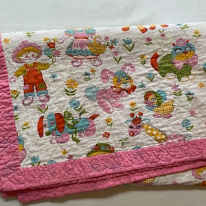 Peut inclure: Une couverture matelassée blanche avec une bordure rose. La couverture présente un motif répété d'animaux de dessin animé colorés et de fleurs.