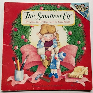May include: A red book cover featuring a green wreath with a pink bow. The book title is "The Smallest Elf" by Annie Ingle, illustrated by Jerry Smath. It is a Random House Pictureback.