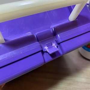 May include: Purple plastic storage case with a white handle and a latch. The case is closed.