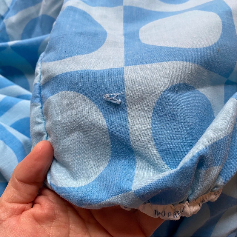 May include: A close-up of a blue and white patterned fabric with a small tear in the fabric. The fabric has a geometric pattern of circles and squares.