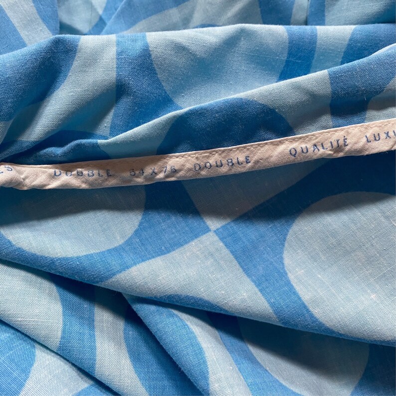 May include: Close-up of a blue and white fabric with a geometric pattern. The fabric has a white label that reads "DOUBLE 54 x 75 DOUBLE QUALIT&Eacute; LUXI".