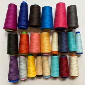May include: A collection of 24 spools of thread in various colours, including red, blue, green, yellow, orange, pink, purple, and black. The spools are arranged in two rows, with 12 spools in each row.