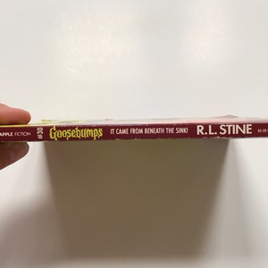 Op de afbeelding: Een rode en gele Goosebumps-boekrug met de titel "It Came From Beneath The Sink!" van R.L. Stine. Het boek is nummer 30 in de Goosebumps-serie.