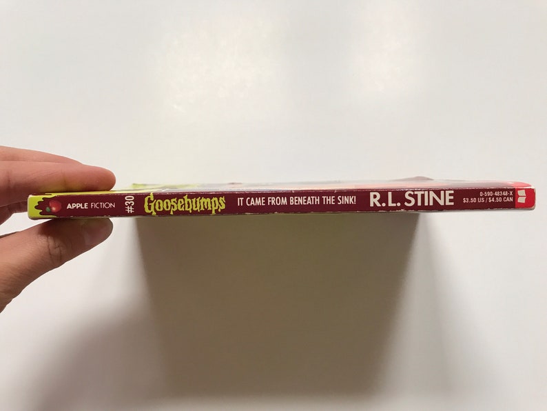 Op de afbeelding: Een rode en gele Goosebumps-boekrug met de titel "It Came From Beneath The Sink!" van R.L. Stine. Het boek is nummer 30 in de Goosebumps-serie.