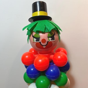 May include: A vintage plastic clown toy. It has a pink face, green hair, and a black top hat with a yellow band. The clown's body is made of red, blue, green, and white spheres.