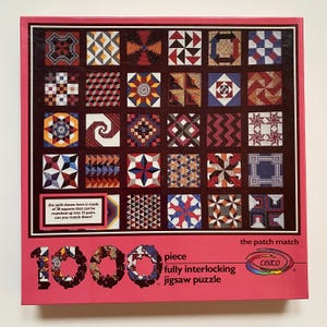 May include: A 1000-piece jigsaw puzzle with a pink border. The puzzle features a quilt pattern with 30 squares in various colors and designs. Text on the box reads "the patch match" and "fully interlocking jigsaw puzzle."