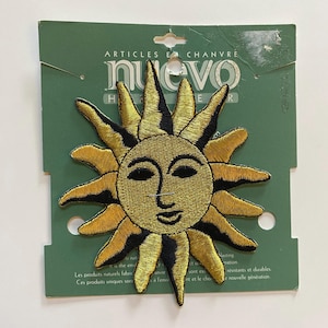May include: A gold embroidered iron-on patch featuring a sun with a smiling face. The patch is on a green card with the text "ARTICLES EN CHANVRE nuevo HEMP WEAR" printed on it.