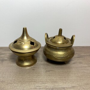 以下が含まれることがあります： 真鍮製の小さな香炉が2つ。1つは蓋と3本の脚が付いた丸いずんぐりした香炉。もう1つは、広い底を持つ高い円錐形の香炉です。