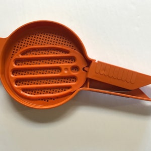 May include: Orange plastic kitchen strainer with a handle and a removable, slotted, strainer insert.