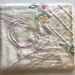 May include: White cotton throw blanket with a pink embroidered design of a large letter C and a floral pattern with pink, yellow, and blue flowers.