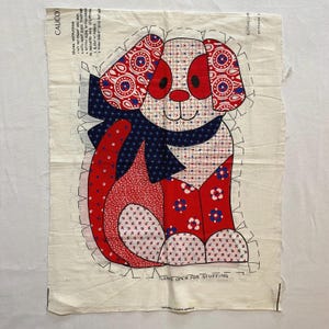 May include: A fabric panel with a pattern of a red, white, and blue dog with a blue bow. The panel is marked with instructions for sewing and cutting. The text on the panel reads "Leave open for stuffing" and "Calico".