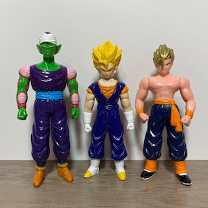 May include: Three plastic action figures standing side by side. The left figure is green-skinned with a white turban and purple outfit. The center figure has spiky yellow hair and a blue outfit. The right figure has blonde hair and blue pants.