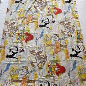May include: A white cotton twin-sized bed sheet with a cartoon print of Wile E. Coyote, Road Runner, and Sylvester the Cat. The sheet features a yellow, orange, and blue color scheme with the text "Beep Beep" repeated throughout.