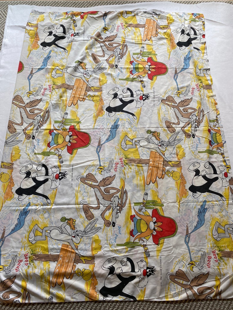 May include: A white cotton twin-sized bed sheet with a cartoon print of Wile E. Coyote, Road Runner, and Sylvester the Cat. The sheet features a yellow, orange, and blue color scheme with the text "Beep Beep" repeated throughout.