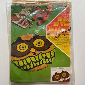 Peut inclure: Un kit de loisirs créatifs pour réaliser un tapis en suivant les numéros. Le kit représente un hibou brun et jaune avec un large sourire. Le kit comprend de la laine de différentes couleurs, une toile et des instructions. Le texte sur l'emballage indique "Columbia Minerva Rugs By The Numbers No Yarn".