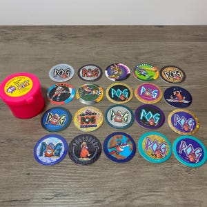 May include: A selection of POGs, circular cardboard game pieces, with diverse designs and the word "POG" visible. A pink plastic container labelled "Canada Caps Playing Starter Kit" is also present. The POGs feature cartoon characters.