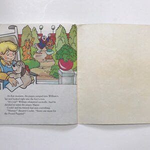 May include: A boy in a wheelchair smiles as a puppy jumps into his lap. The puppy is holding a white envelope. The boy is wearing a yellow shirt and blue pants. The puppy is brown and white. The background shows a park with green trees and a red ball.