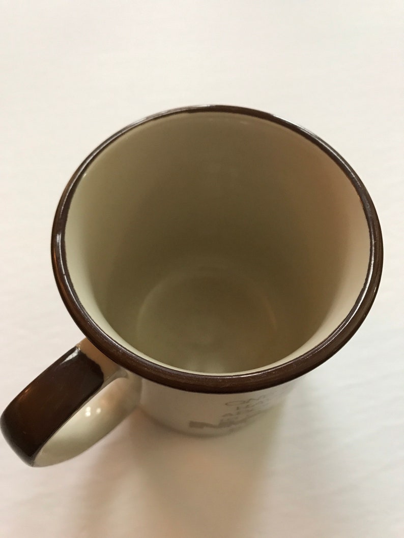 K&ouml;nnte beinhalten: Eine braune Keramiktasse mit wei&szlig;em Innenraum und braunem Henkel. Die Tasse hat einen braunen Rand und ein braunes Band um den Boden. Die Tasse ist leer.