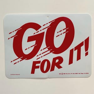 May include: White sign with red text that reads "GO FOR IT!" with a copyright notice at the bottom that reads "[83] 1964 HAL Ent. P.O. Box 20667, San Diego, CA 92120"