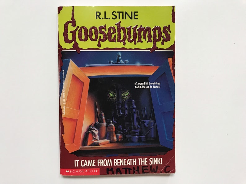 Op de afbeelding: Een Goosebumps-boekomslag met een rode titel met druppelend bloed, "Goosebumps", en een gele achtergrond. De omslagillustratie toont een gootsteen met de groene ogen van een monster die onder de gootsteen vandaan kijken. De titel van het boek is "It Came From Beneath The Sink!" met de naam van de auteur, "R.L. Stine", bovenaan. Het boek is uitgegeven door Scholastic.
