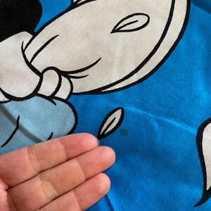 May include: A blue t-shirt with a white cartoon character on it. The character has a black outline and is smiling. The t-shirt has a small green stain on it.