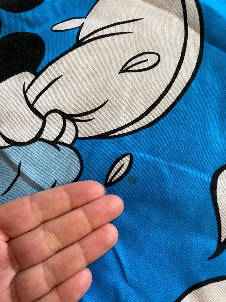 May include: A blue t-shirt with a white cartoon character on it. The character has a black outline and is smiling. The t-shirt has a small green stain on it.