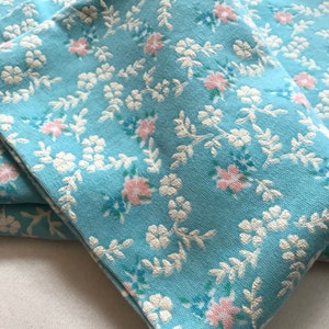 May include: A stack of four blue fabric napkins with a white and pink floral pattern.