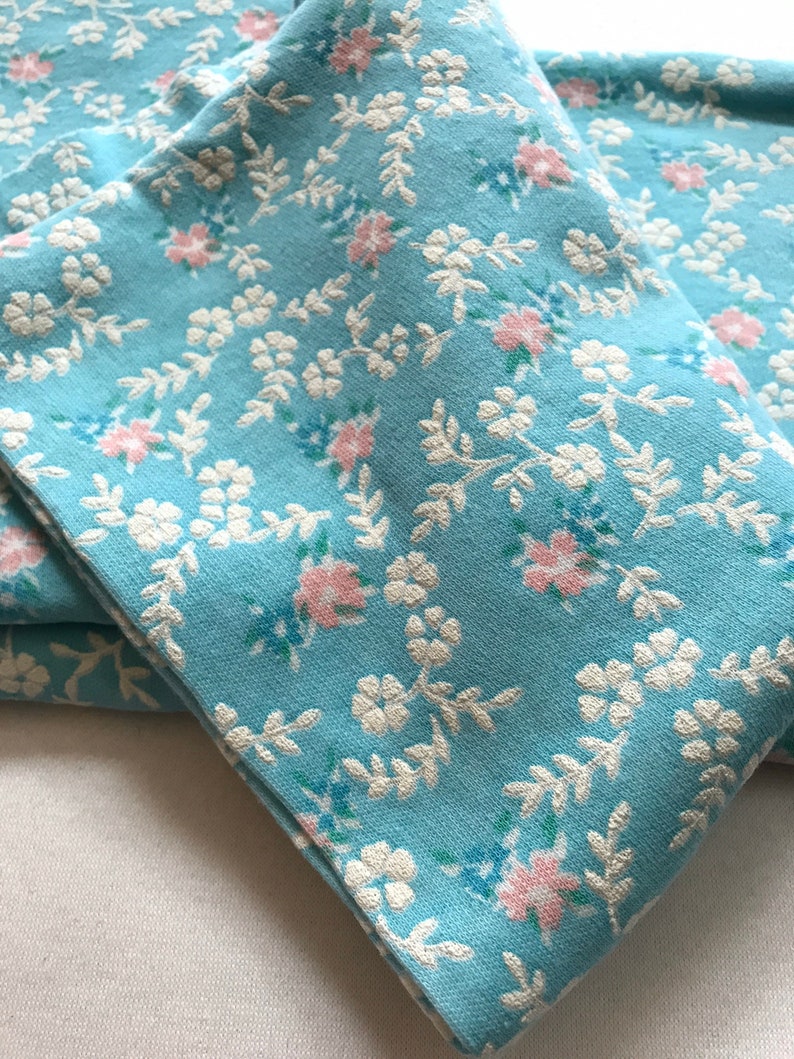 May include: A stack of four blue fabric napkins with a white and pink floral pattern.