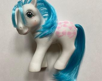Puede incluir: Un pony blanco con pelo azul y un diseño estampado rosa y blanco en su espalda.