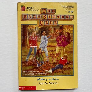 May include: Cover of a paperback book titled "The Baby-Sitters Club: Mallory on Strike" by Ann M. Martin. The cover features a group of four girls in a fall setting, raking leaves. The book is number 47 in the series.